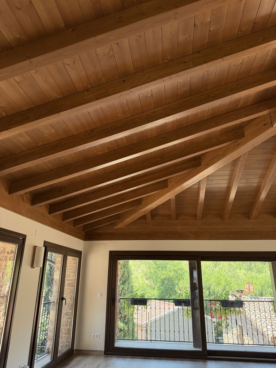 Salón con vigas de madera y grandes ventanales, obra de Montajes Depedro